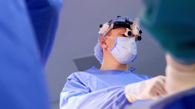 Cerrahi hoparlör takan beyaz erkek cerrah metal bir alet kullanıyor. Düşük açı. Operasyonda çalışan bir beyin cerrahının portresi.