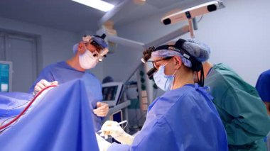 Kafkasyalı yetişkin bir kadın doktor farlar ve ameliyat lüleleri takıyor. Beyin ameliyatında çalışıyor. Yan görüş. Modern hastanede beyin cerrahisi gerçekleştirildi.