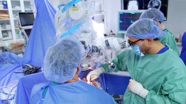 Doktorun mikroskoba bakıp operasyonu yürüttüğü görünümü. Cerrahın asistanı tuz çözeltisini püskürtür..