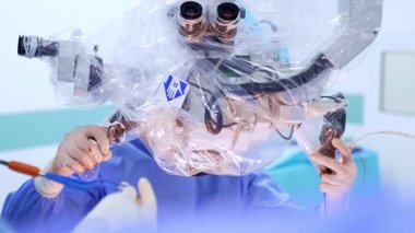 Kan lekeli eldiven giyen tanınmayan doktor hastanın üzerinde mikroskop taşıyor. Beyin ameliyatı..