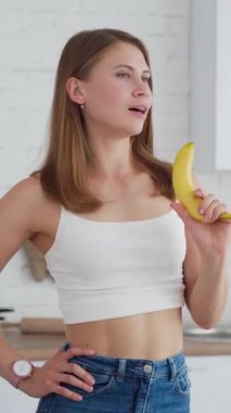 Kadın muzla eğleniyor. Genç bir bayan mutfakta taze meyve tutuyor. Evde gülümseyen güzel bir kız. Sağlıklı gıda kavramı. Dikey video