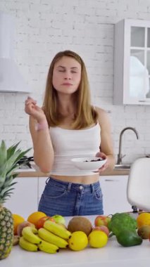 Modern mutfakta güzel bir kadın. Masada organik meyve ve sebze var. Vejetaryen yemeği yiyen genç bir kadın. Sağlıklı beslenme konsepti. Dikey video