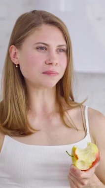 Elmalı genç bir kadının yarım boy portresi. Güzel kız mutfakta taze organik meyve yiyor. Sağlıklı yiyecekler. Diyet konsepti. Dikey video