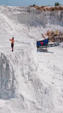 Beyaz tepenin kenarındaki kaslı adam. Tişörtsüz sporcu, güçlü vücudunu kayalık kanyonda doğal yaz arka planında gösterir. İHA görüntüsü. Dikey video