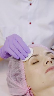 Bir uzman, müşteriye kozmetolojinin merkezindeki alın bölgesinde mezoterapi enjeksiyonu yapıyor. Modern kozmetoloji. Cilt nemlendirme prosedürü Dikey video