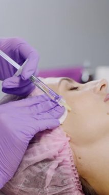 Bir müşteri kuaförde farklı kozmetik ürünlerinin arka planına iğne vurularak mesoterapi görüyor. Güzellik endüstrisi. Dikey video