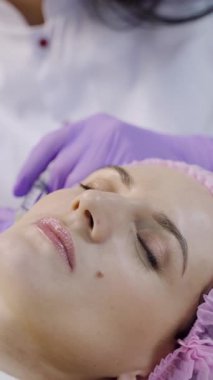 Güzel bir kadın kozmetolojide kozmetik uzmanı ile bir kanepede uzanıyor. Dikey videoyu kapat