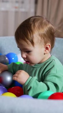 Havzada parlak renkli plastik toplarla oturan güzel erkek bebek. Mutlu çocuk heyecanla el sallıyor. Kara kedi şaşkın ve arka planda biraz şok olmuş görünüyor. Dikey video