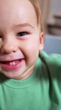 Sevimli bir şekilde gülümseyen oğlan kameraya bakıyor ve iki alt dişini gösteriyor. Heyecanlı çocuk elini kameraya dayayıp gülüyor. Dikey video