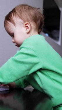 Bir yaşında güzel bir çocuk merdivenlerde telefonla oynuyor. Odaklanmış çocuk aleti elinde döndürüyor ve merakla inceliyor. Dikey video