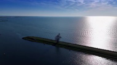 Merkemeer Gölü 'nün barajında çömelmiş bir adamın metal heykeline yaklaşıyoruz. Güneş gölün yüzeyine yansıyor. Hava görüntüsü. Lelystad, Hollanda.
