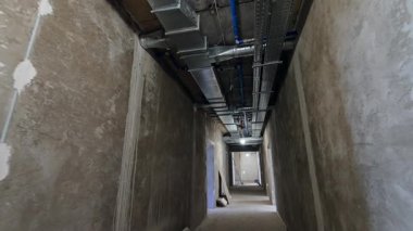 İnşaat binasındaki uzun koridorun gri duvarları. Tavandaki boruların düşük açılı görüntüsü.