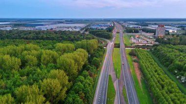 Otoyoldaki yeşil alanlar, NL. Hollanda 'da günbatımında yemyeşil ve sanayi bölgeleriyle çevrili bir otoyolu hava manzarası yakalar..