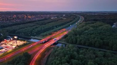Alacakaranlıkta Hollanda yolları. Bir günbatımı, Hollanda 'nın verimli banliyölerinden geçen ve kentsel ve doğal güzellikleri harmanlayan bir otoyolu aydınlatıyor..