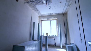 İnşaat alanına boru döşeme. İnşaat altındaki bir odada metal boru işi ve geniş pencereli açıkta duran duvarlar doğal ışık alıyor..