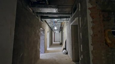 İnşaat alanı boş. İnşaat alanında uzun, çıplak bir koridor, açıkta duran duvarlar ve aydınlatma armatürleri..