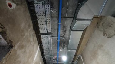 Endüstriyel tavanda açıkta duran borular. Endüstriyel ortamlar, açık metal yapılar, mavi borular ve desenli tavana karşı havalandırma kanalları gösteriyor..