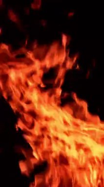 Ateşten alevler karanlıkta farklı yönlere hızla ilerler. Ateş dilleri uçuyor. Kapatın. Dikey video