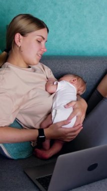 Kafkasyalı anne iş ve çocuk bakımını birleştiriyor. Silahlı çocuklu bir kadın dizüstü bilgisayarda çalışıyor. Dikey video