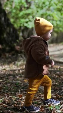 Beyaz, şirin bir bebek parkta kuru yaprakların arasında yürüyor. Sonbaharda yürüyüş yapan bir çocuk. Dikey video