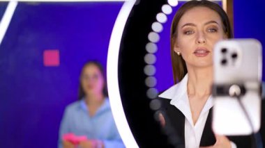 Uzun saçlı, beyaz, güzel bir kadın hafif yüzüklü kameraya bakıyor. Blogcu elleriyle tutkuyla el kol hareketi yapıyor. Kadın, arkasında bir kızın durduğu cam duvarı işaret etmek için döner..