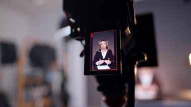 Beyaz tenli esmer, profesyonel kameranın önünde konuşuyor ve el kol hareketi yapıyor. Kapatın. Bulanık arkaplan.