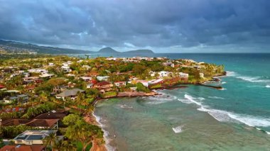 Okyanus kıyısındaki resimli yeşil yerleşim bölgesi. Şehrin üzerindeki gri bulutlar gökyüzünü kapladı. Honolulu, Hawaii, ABD. Hava görünümü.
