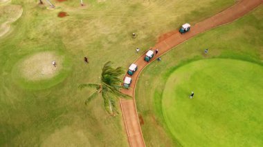 Rüzgarlı bir günde yeşil sahada golf arabaları ve golf oyuncuları. Honolulu, Hawaii, Waikiki 'de lüks bir spor. Üst görünüm.