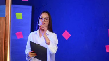 Ofis beyin fırtınası oturumu. Bir grup üyesi, mavi duvardaki renkli yapışkan notlarla çevrili beyin fırtınası oturumuna aktif olarak katılır..