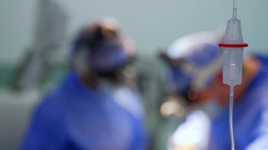 Teslimat tezgahının içinde sıvı damlıyor. Kapatın. Ameliyat yapan iki sıhhiyenin bulanık görüntüsü.