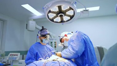 Bir hastayı ameliyat eden iki cerrahla arama mesafe koymak. Kadın ameliyathane hemşiresi, cerrahi bölümünden bir alet alır..