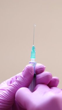 Bir kozmetolojistin yakından görüntüsü, elinde yüz enjeksiyonlarını gençleştirmek için şırıngayla eldiven tutuyor. Dikey video