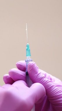 Bir kozmetolojistin yakından görüntüsü, elinde yüz enjeksiyonlarını gençleştirmek için şırıngayla eldiven tutuyor. Dikey video