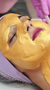 Genç bir kadın güzellik salonunda yüz aşısı yaptırıyor. Yaşlanma, gençleşme ve hidrasyon prosedürleriyle yüzleş. Estetik kozmetoloji. Dikey video