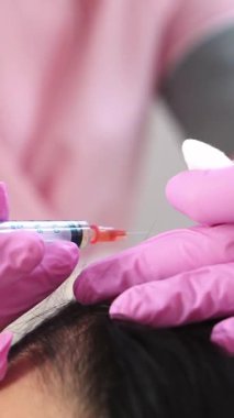 Yakışıklı bir kadın kafasına bir iğne vurulur. Mezoterapi kavramı. Saçı güçlendirmek ve büyümelerini dikey görüntülemek için itme