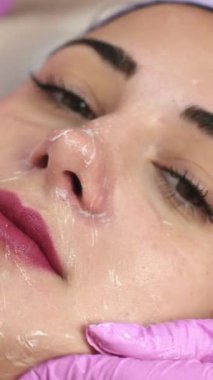 Güzeller güzeli genç bir kadın güzellik salonunda kozmetik maske takıyor. Kozmetik yüz tedavisi. Cilt bakımı dikey video kavramı