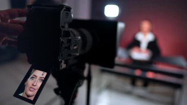 Üç ayaklı bir kameranın önünde gülümseyen beyaz güzel bir kadının yüzü. Erkek eller kameranın düğmesini değiştiriyor. Bulanık arkaplan.