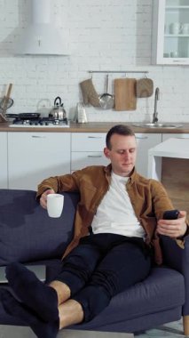 Evde akıllı telefon kullanan bir adam. Genç adam koltukta oturuyor, cep telefonu kullanıyor.