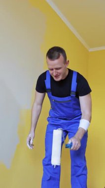 Duvarları silindirle boyayan adam. Üniformalı işçi duvarları boya silindiriyle boyuyor.