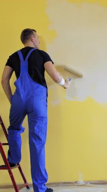 Boya silindirli bir inşaatçı. İnşaat müteahhidi. Duvarı tekerlekli fırçayla boyuyor.