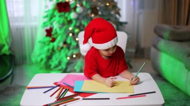 Noel 'de çocuk işçiliği süslemesi. Noel Baba şapkası takan küçük bir çocuk Noel ağacının yanında ışık ve süslemelerle süslenmiş..