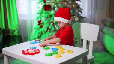 Xmas 'ta blokları olan bir çocuk. Kırmızı tişörtlü küçük bir çocuk ışıklarla süslenmiş bir Noel ağacının yanında renkli bloklar oluşturuyor..