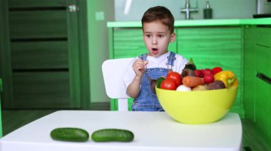 Çocuk parlak ürünleri keşfediyor. Küçük bir çocuk masada oturmuş, çeşitli meyve ve sebzelerle dolu büyük bir kaseyi izliyor, anın tadını çıkarıyor..