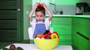 Çocuk mutfakta sağlıklı yemek hazırlıyor. Tulumlu bir çocuk, parlak bir mutfakta bir kase taze sebzeyle domateslerle oynuyor..