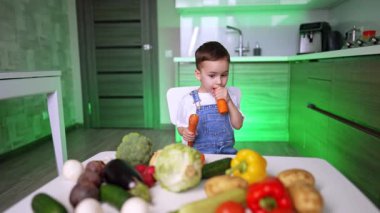 Sağlıklı yiyecekleri keşfeden bir çocuk. Genç bir çocuk taze sebzelerle bir masada oturuyor, modern bir mutfak ortamında farklı renkleri ve dokuları keşfediyor..