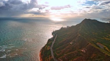 Pasifik Okyanusu kıyısındaki engebeli dağlar. Su yüzeyinde çok az yelkenli var. Günbatımında Oahu, Hawaii, ABD sahilindeki hava manzarası..