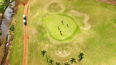 Golf arabalarıyla yeşil çimlerin üzerinde duran dört adam var. Hawaii, ABD 'de golfçülere en iyi bakış açısı.