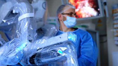 Robot cerrah minimal istila operasyonu gerçekleştiriyor. Gözlüklü doktor makinenin arkasında duruyor. Doktorun arkasındaki ekranda ameliyatı gösteriyor..