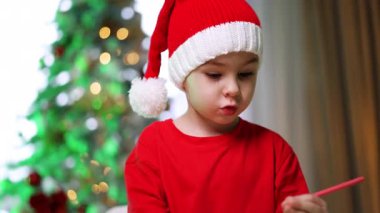 Noel Baba şapkalı sevimli çocuk pembe bir kalem tutuyor. Evde resim yapan bir erkek bebeğin portresi. Kapat..