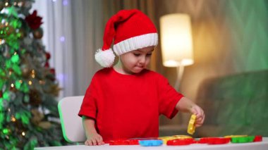 Kırmızı Noel Baba şapkalı ve tişörtlü sevimli bebek masada duruyor. Tatlı çocuk oyun oynuyor..
